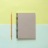 white spiral notebook beside orange pencil